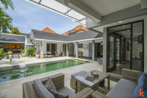 Elegant and airy indoor living space in a Balinese villa, combining a lounge, dining area, and kitchen, adorned with traditional artwork and high vaulted ceilings.